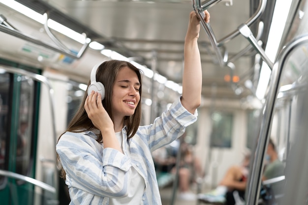 写真 地下鉄の電車の中でワイヤレスイヤホンで音楽を聴いているのんきなミレニアル世代のかわいい女の子の乗客