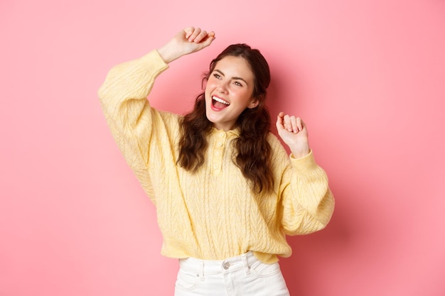 Photo carefree party girl dancing and having fun looking up singing along and looking up posing against pi...