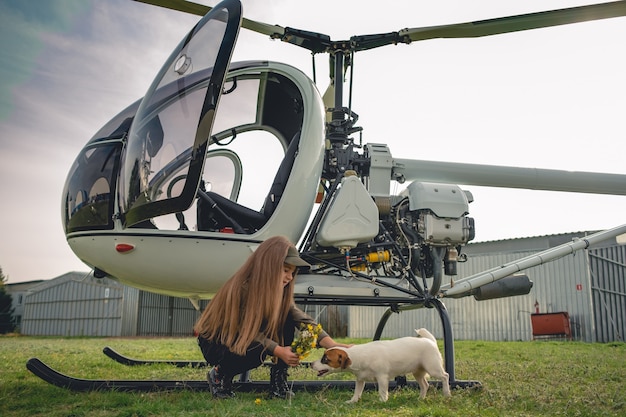 Беззаботная девочка-подросток играет с собакой возле вертолета