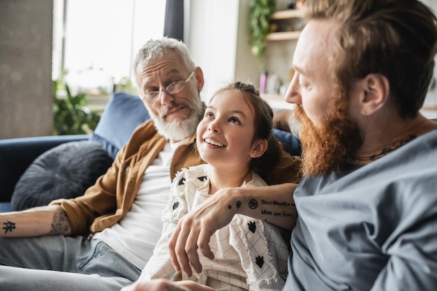 Carefree preteen girl talking to gay parents in living room