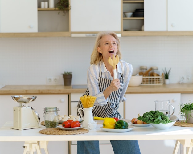 Donna anziana spensierata che si diverte mentre cucina in una cucina moderna e leggera a casa