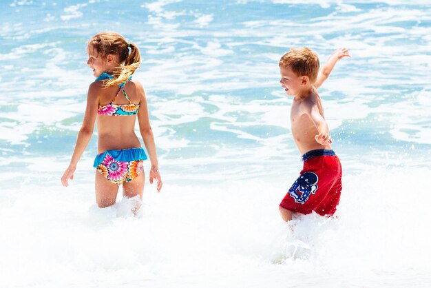 Photo carefree siblings standing in sea during sunny day