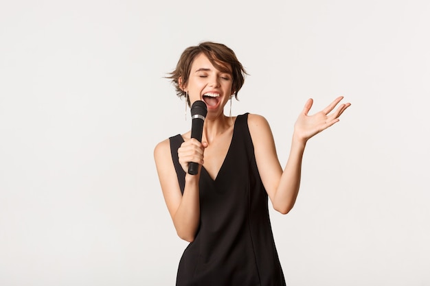 carefree singer performing over white. beautiful woman singing into microphone, standing white background.