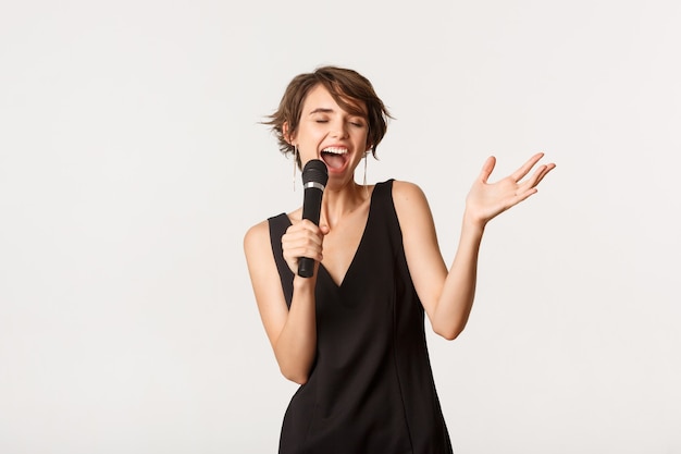 Carefree singer performing over white. Beautiful woman singing into microphone, standing white background.