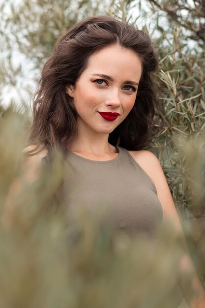 Foto donna alla moda spensierata con labbra rosse e capelli lunghi in piedi vicino all'albero nel giardino verde