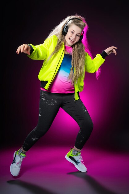 Carefree teenager girl using headphones with music dancing having fun jumping in casual sportswear