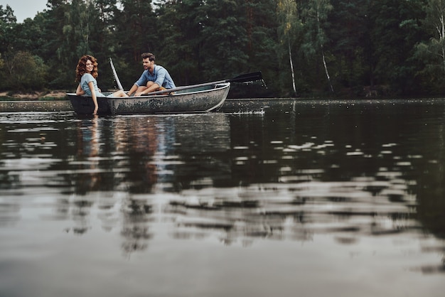 Беззаботные выходные. Красивая молодая пара наслаждается романтическим свиданием во время гребли на лодке