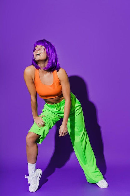 Carefree woman dancer wearing colorful sportswear having fun against purple background