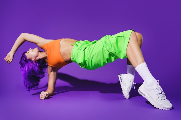 Carefree woman dancer wearing colorful sportswear performing against purple background