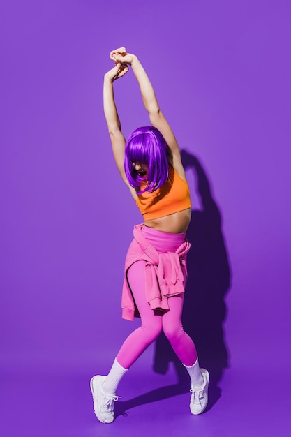 Carefree woman dancer wearing colorful sportswear performing against purple background