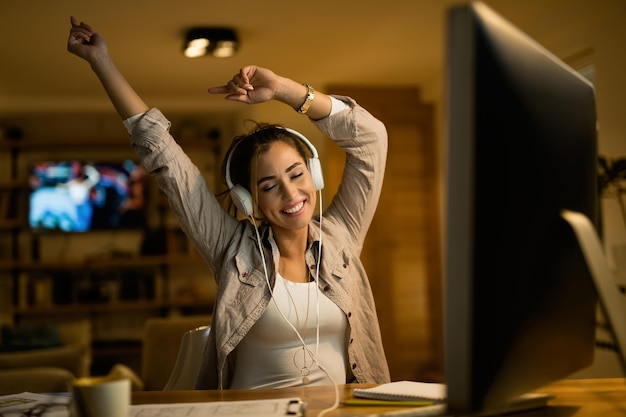 Carefree woman listening music with eyes closed while using computer in the evening at home