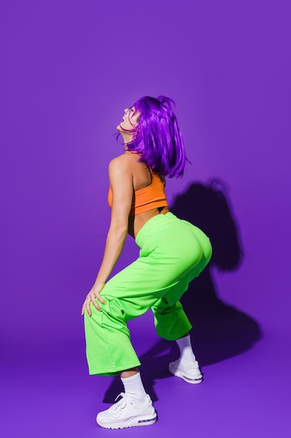 Donna spensierata che indossa abiti sportivi colorati twerking su sfondo viola