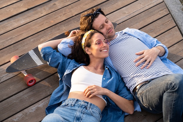 Беззаботная молодая пара, лежа на скейтборде, обнимается, наслаждается закатом вместе, отношениями и образом жизни