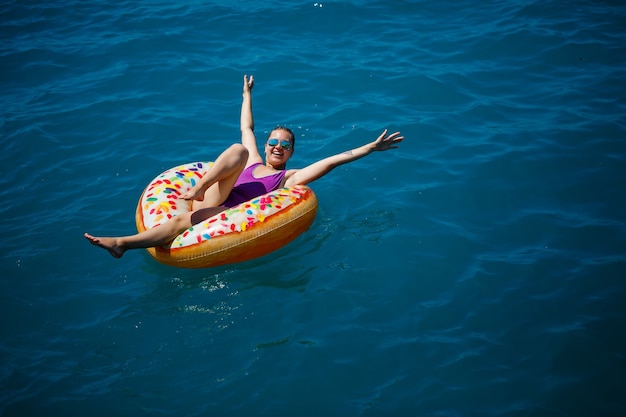Фото Беззаботная молодая девушка женщина, наслаждающаяся расслабляющим днем в море, плавая на надувном кольце, вид сверху. концепция отдыха на море