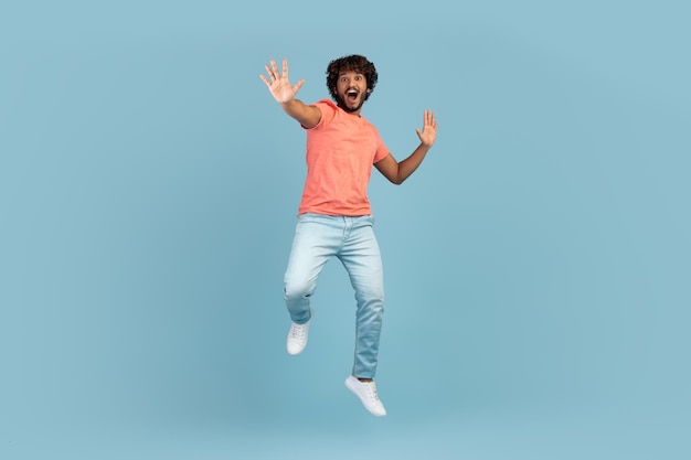 carefree young indian man jumping over blue