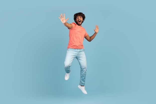 Carefree young indian man jumping over blue