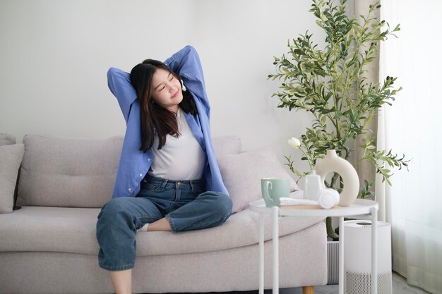 Photo carefree young woman reading on couch and stretching arms in cozy living room