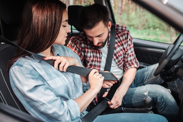 注意深い人々が車に座って、スタート前にシートベルトをロックしています。女の子が左下を見ている間、男は下を見ています。