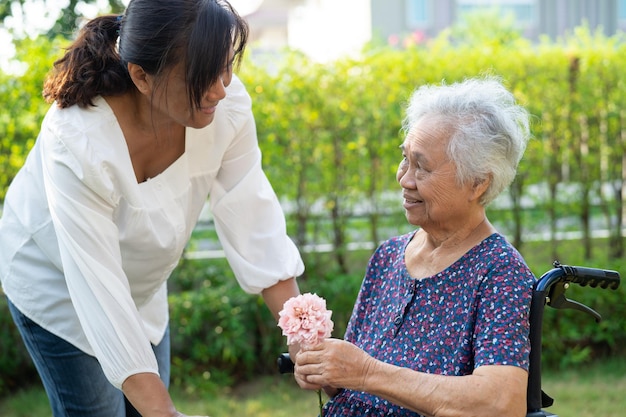 Caregive parla e aiuta una donna anziana asiatica che tiene il sorriso dei fiori e felice nel giardino soleggiato