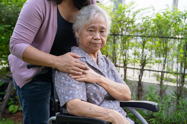 介護者の娘は、公園で電動車椅子でアジアのシニアまたは高齢の老婦人女性を助けます。