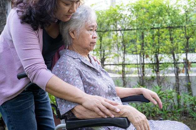 Caregiver daughter help Asian senior or elderly old lady woman on electric wheelchair in park