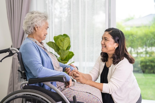 Caregiver daughter help Asian senior or elderly old lady woman sitting on wheelchair and wearing a face mask for protect safety infection Covid19 Coronavirus