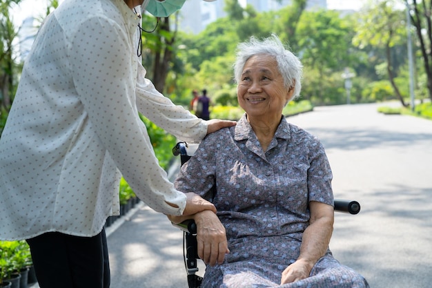 介護者の助けとケア公園で車椅子に座っているアジアの高齢者または高齢の老婦人女性患者健康的な強力な医療の概念