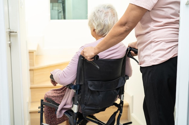 Caregiver help asian or elderly old woman sitting wheelchair support up the stairs in home