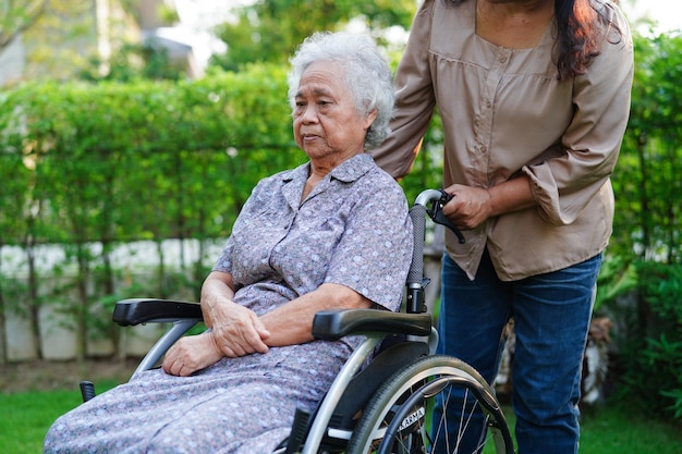 Caregiver help Asian elderly woman disability patient sitting on wheelchair in park medical concept