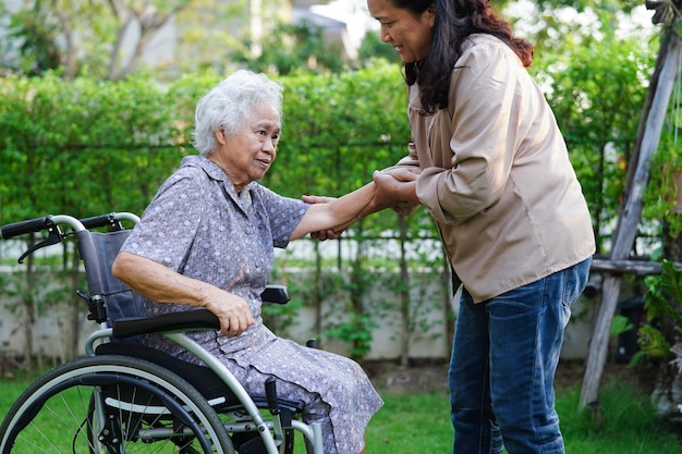 Caregiver help Asian elderly woman disability patient sitting on wheelchair in park medical concept