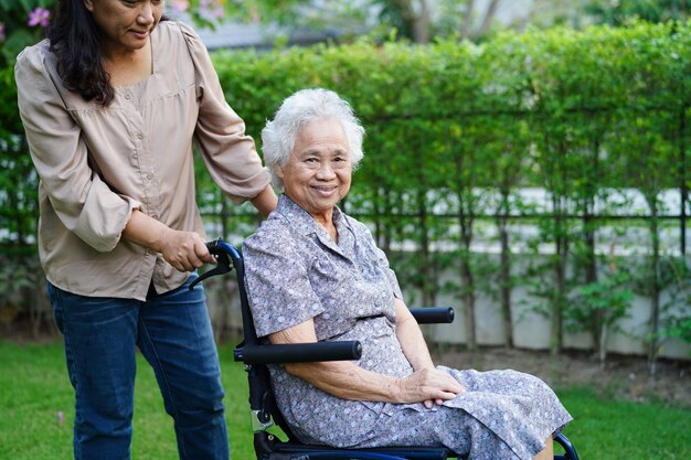 Caregiver help Asian elderly woman disability patient sitting on wheelchair in park medical concept