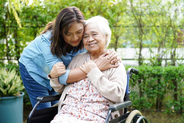 Caregiver help Asian elderly woman disability patient sitting on wheelchair in park medical concept