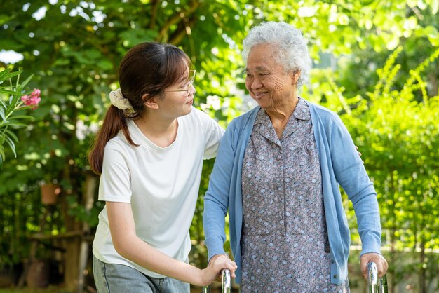 Caregiver help Asian elderly woman patient walk with walker in park healthy strong medical concept