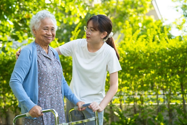 Caregiver help Asian elderly woman patient walk with walker in park healthy strong medical concept