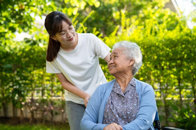 介護者の助けとケアアジアの年配の女性は、幸せな新鮮な休日に公園を歩きながら、健康状態の良いウォーカーを使用します