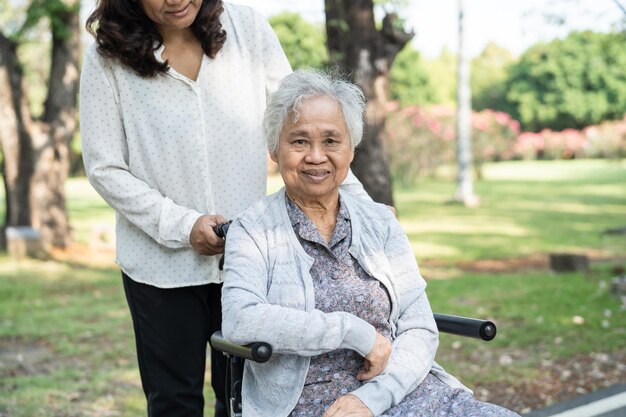 Assistenza e cura del caregiver paziente asiatico anziano o anziano donna seduto e felice sulla sedia a rotelle nel parco sano concetto medico forte