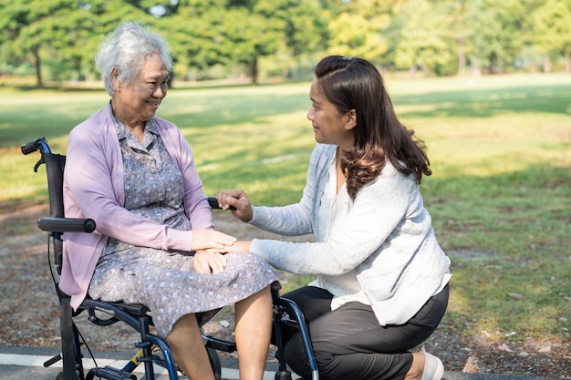간병인의 도움과 보살핌 아시아 노인 또는 노인 여성 환자가 공원에서 휠체어에 앉아 행복하고 건강한 강한 의료 개념