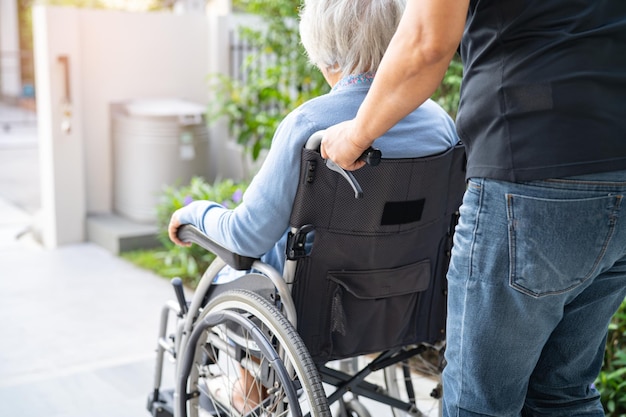 Caregiver help and care Asian senior or elderly old lady woman patient sitting on wheelchair at nursing hospital ward, healthy strong medical concept