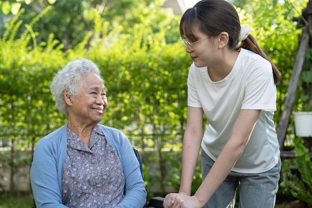 Caregiver help and care Asian senior or elderly old lady woman patient sitting on wheelchair in park healthy strong medical concept