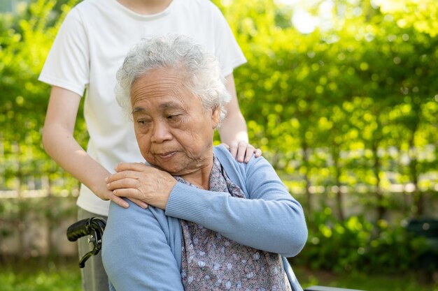 Caregiver help and care Asian senior or elderly old lady woman patient sitting on wheelchair in park healthy strong medical concept