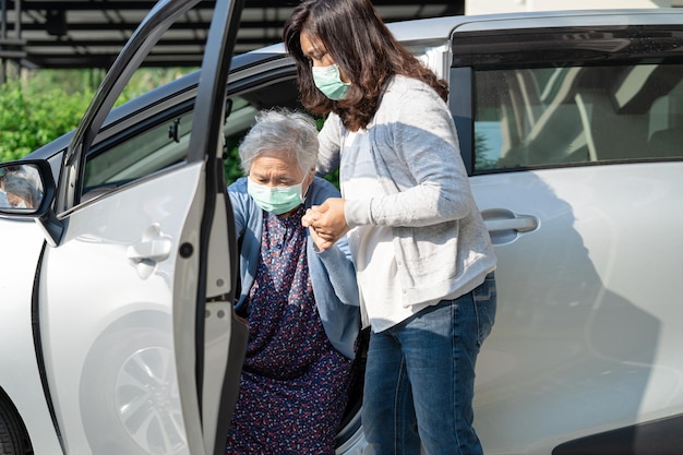 車椅子に座っているアジアの高齢女性を介護者が助け、車に乗る準備をするのをサポートする