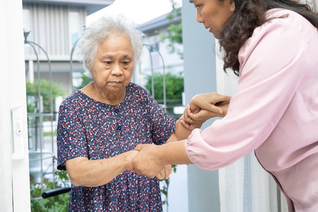 Caregiver help and support asian senior woman while walking stepping up to the door of the house