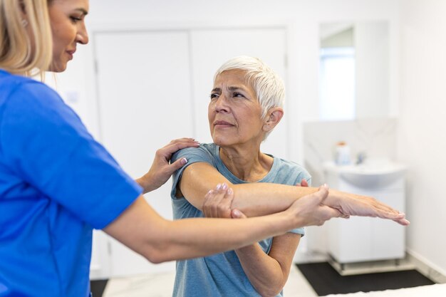 Caregiver helping contented senior woman exercise at clinic rehab for elder senior medical care elder woman returning to good state of health