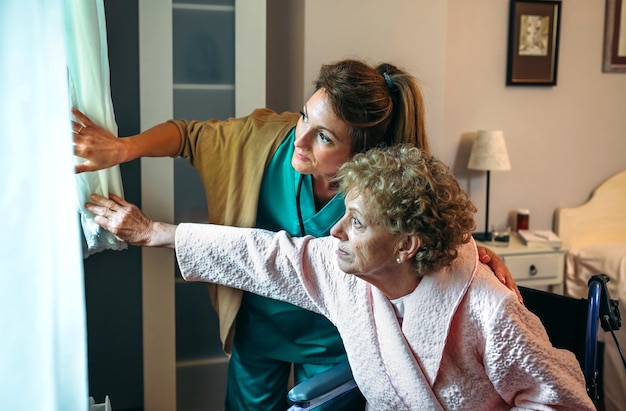 Photo caregiver showing the view through the window to an elderly patient in a wheelchair