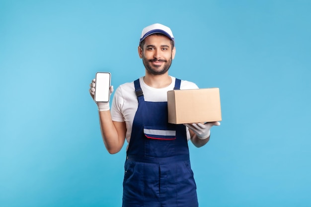 Cargo tracking mobiele app Courier man in uniform met kartonnen doos en mobiele telefoon met blanco display mock up voor expresverzending adverteren online levering bestelling indoor studio shot geïsoleerd