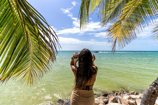 緑の水とヤシの木のあるカリブ海のビーチと、メキシコのカンクンで水を見ている女性