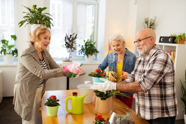 Caring about flowers. Nice happy woman smiling while spraying the flower with water