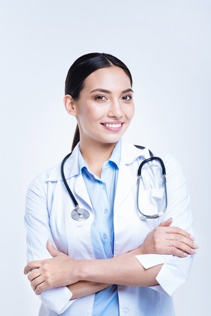 Caring about your health. Pleasant cheerful female doctor with a stethoscope around her neck folding her arms across her chest and smiling