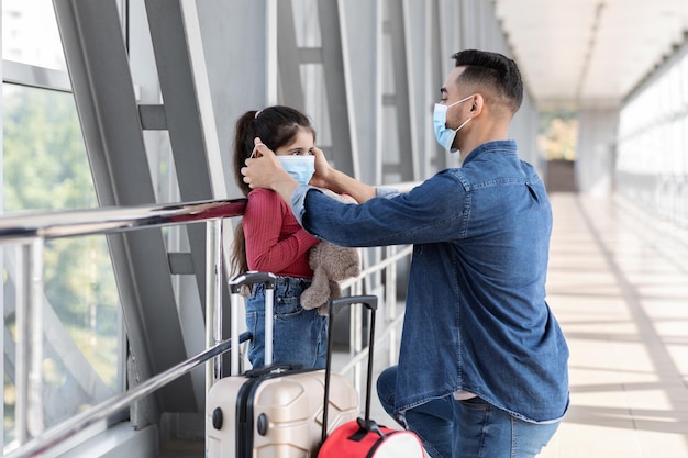 Caring arab father wearing protective medical mask to his daughter at airport