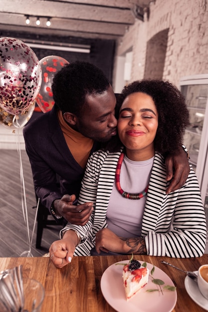 Caring boyfriend. Nice positive man kissing his girlfriend while congratulating her on her birthday